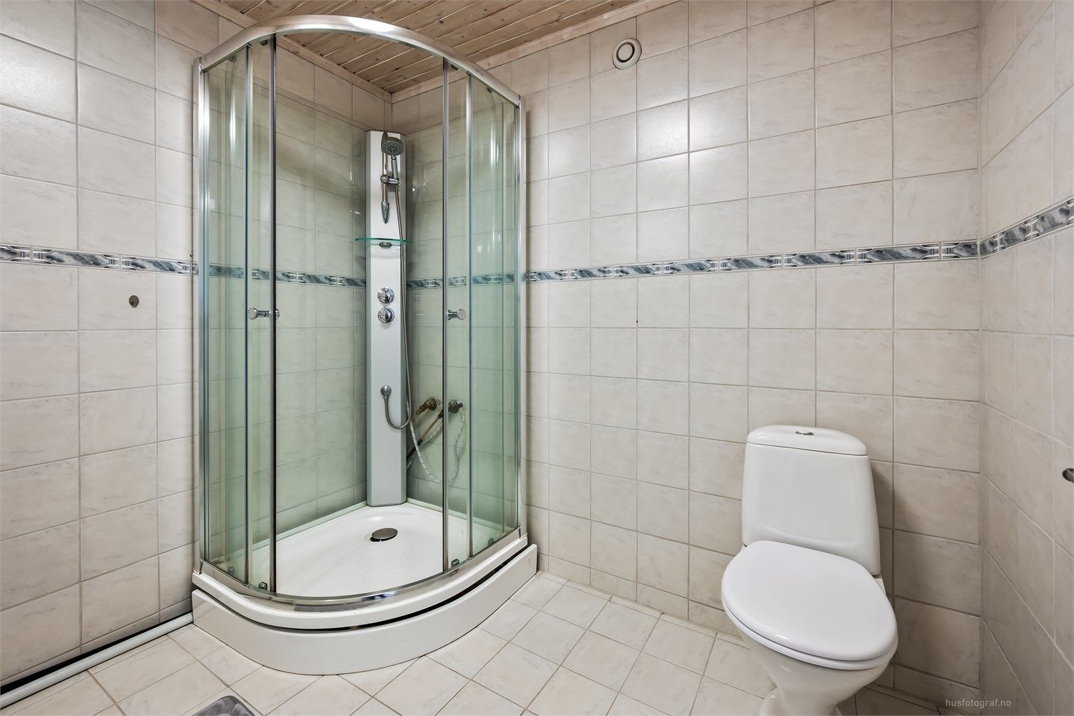 Badet er flislagt og har toalett og et romslig dusjkabinett.
