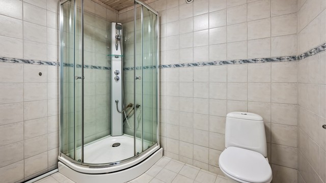 Badet er flislagt og har toalett og et romslig dusjkabinett.