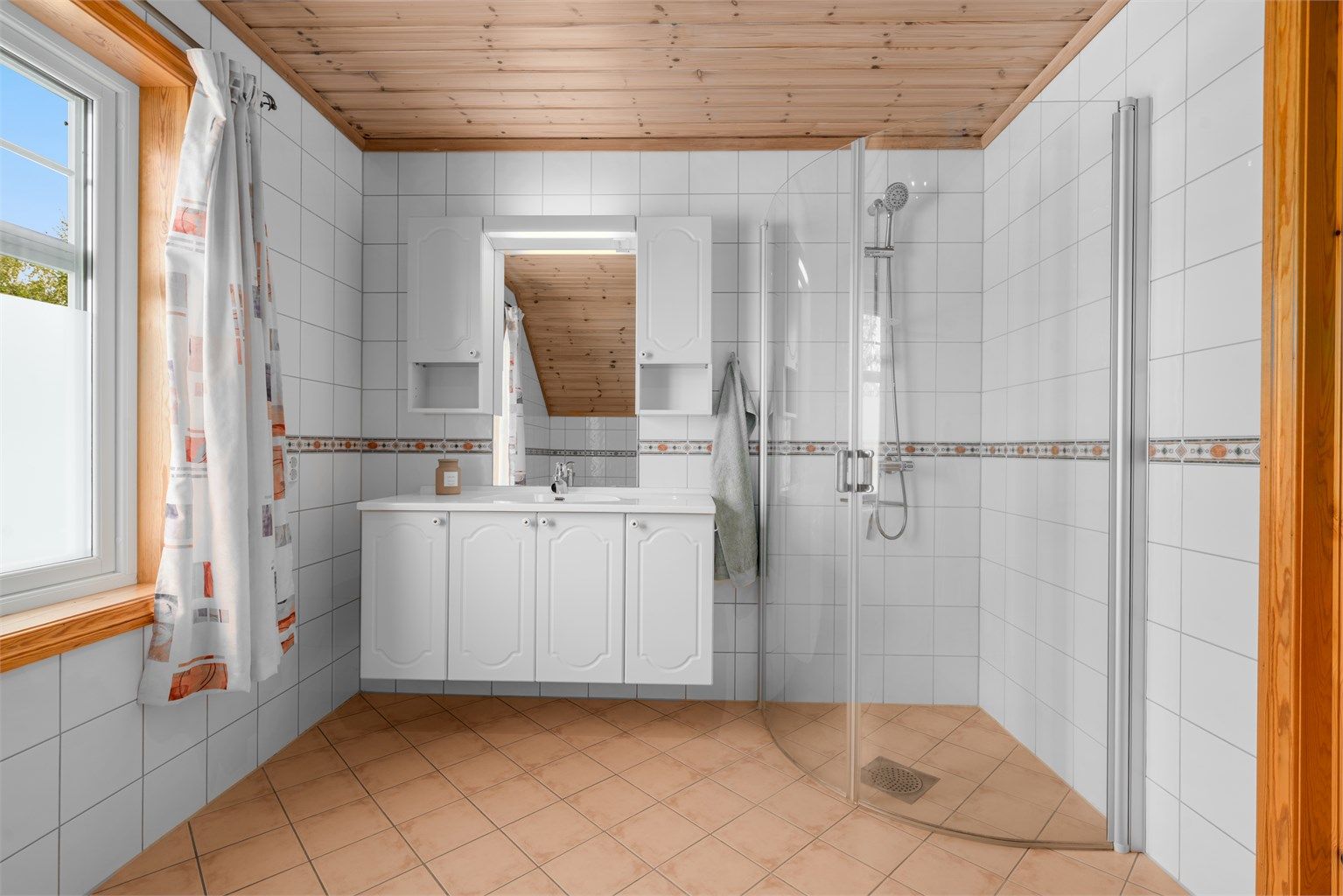 Badet er utstyrt med dusjhjørne og servant med innredning.