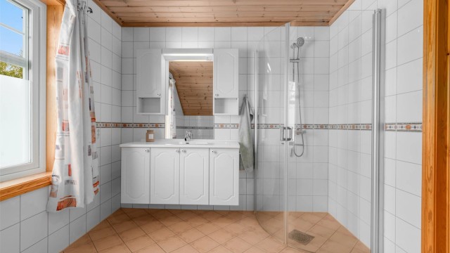 Badet er utstyrt med dusjhjørne og servant med innredning.