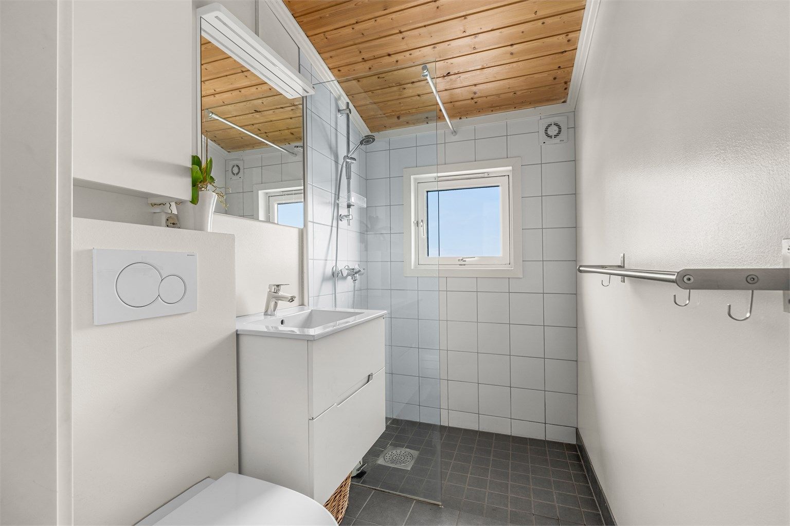 Pent delvis flislagt bad med gulvvarme, servantskap med speil og lys, vegghengt toalett og dusjhjørne. 