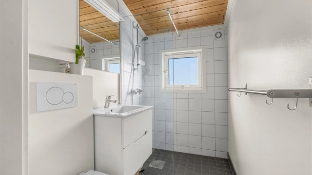Pent delvis flislagt bad med gulvvarme, servantskap med speil og lys, vegghengt toalett og dusjhjørne.