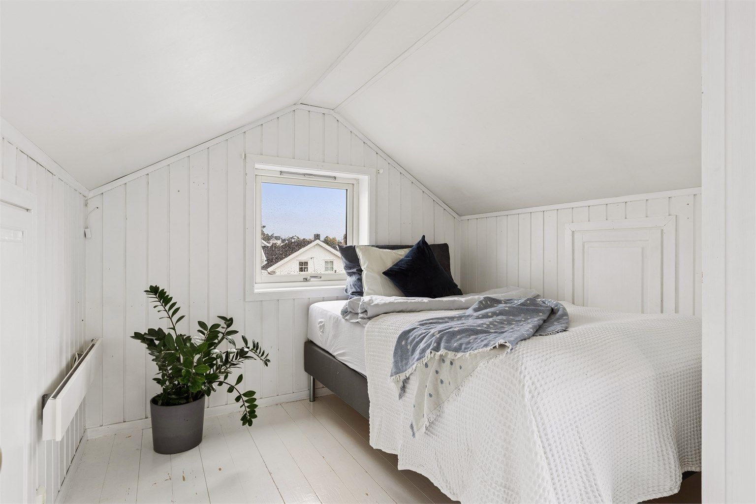 Soverom i loftsetasjen med hvitmalt trepanel og vindu på gavlvegg.
