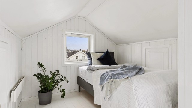Soverom i loftsetasjen med hvitmalt trepanel og vindu på gavlvegg.