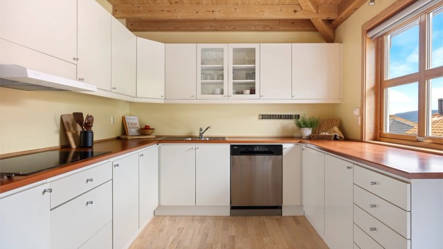 Tidløst kjøken fra byggeår med glatte fronter og benkeplate med laminert overflate. Kjøkkenet er utstyrt med integrert stekeovn og platetopp, samt frittstående oppvaskmaskin og kjøleskap.