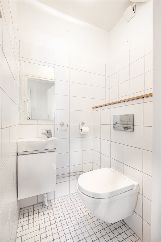 Gjestetoalettet har praktisk plassering i tilknytning til entréen. Toalettrommet har vegghengt innredning med heldekkende servant og vegghengt toalett med innebygget sisterne.