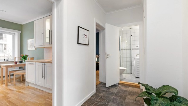 Entréen er plassert i midten av leiligheten og har adkomst til alle rommene. Til høyre for baderommet er det et innbygget skap med plass til sko, jakker og støvsuger.