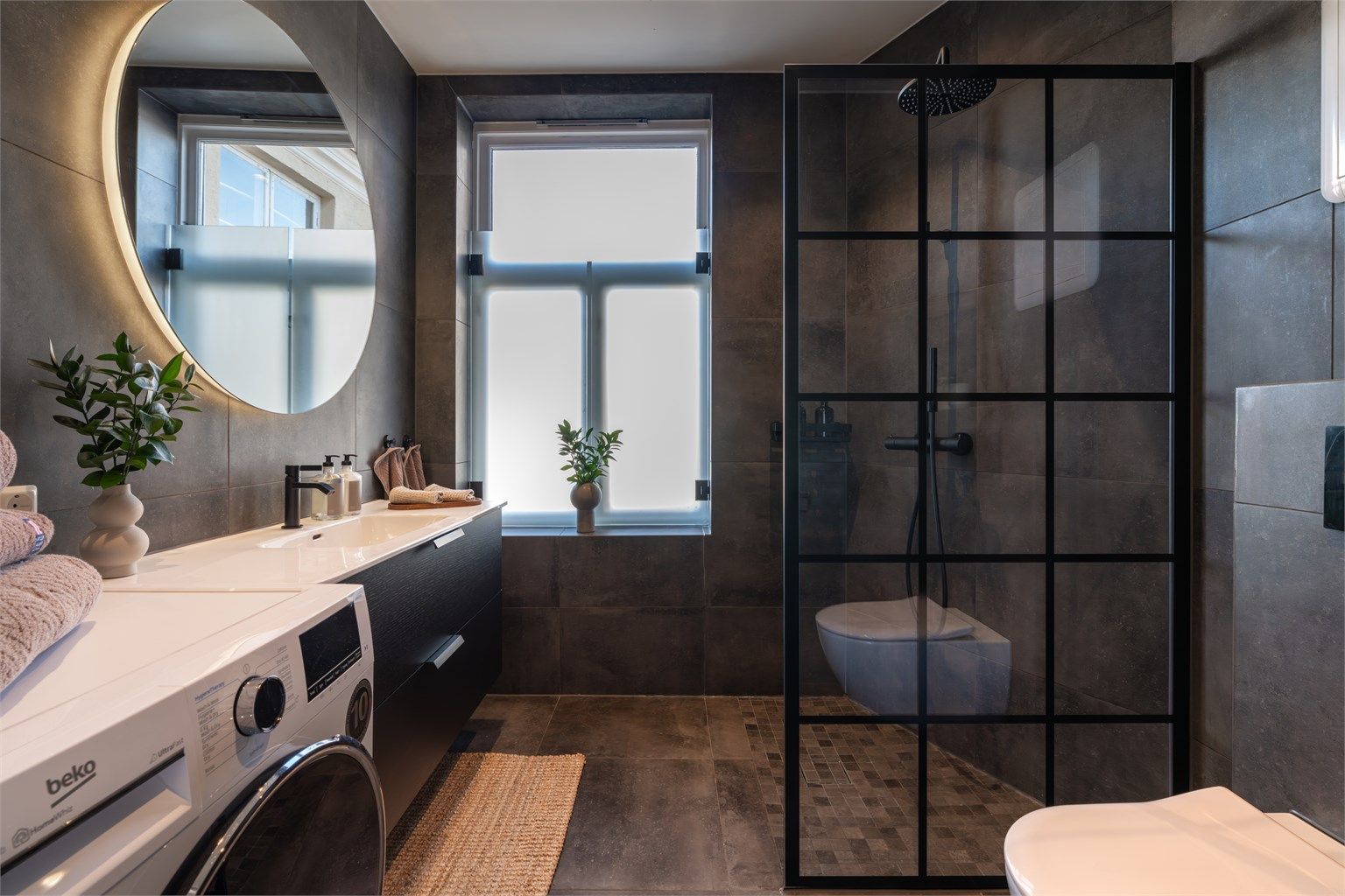 Leiligheten har et romslig bad fra 2021 med store, mørke fliser og delikat innredning som gir en spafølelse i hverdagen. 