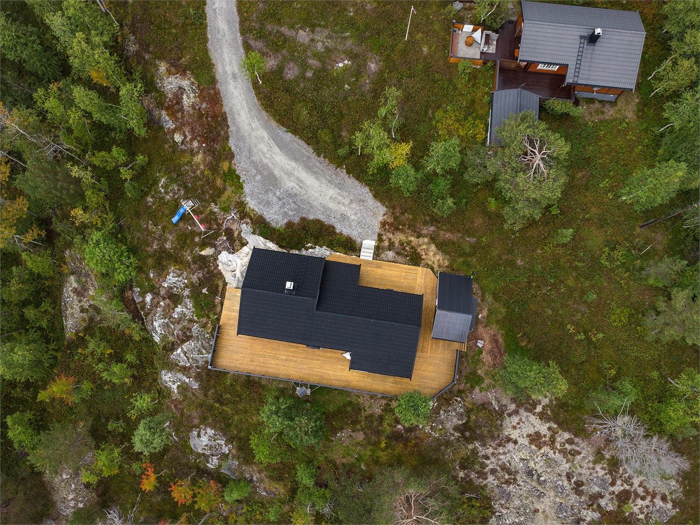 Hyttetomten ligger usjenert til i terrenget med terrassedekke rundt hytten.