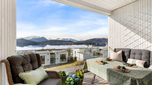 Balkongen har terrassebord på gulvet, rekkverk i glass og metall, samt utelys og stikkontakt