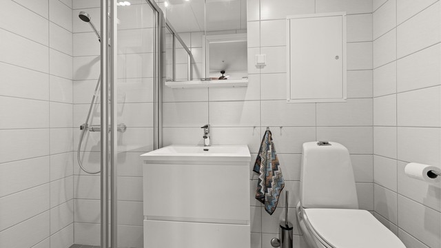 Badet har dusjhjørne, vegghengt toalett og speilskap.