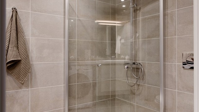 Dusjhjørne med innfellbare glassdører og dusjarmatur med både hånddusj og regndusj.