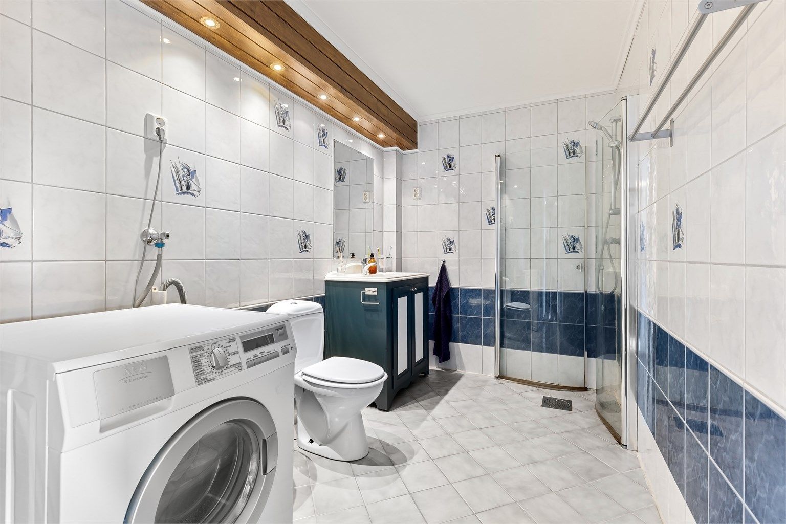 Badet har flislagt gulv med gulvvarme, dusjhjørne og opplegg for vaskemaskin.