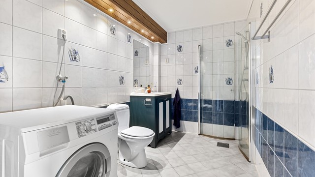 Badet har flislagt gulv med gulvvarme, dusjhjørne og opplegg for vaskemaskin.