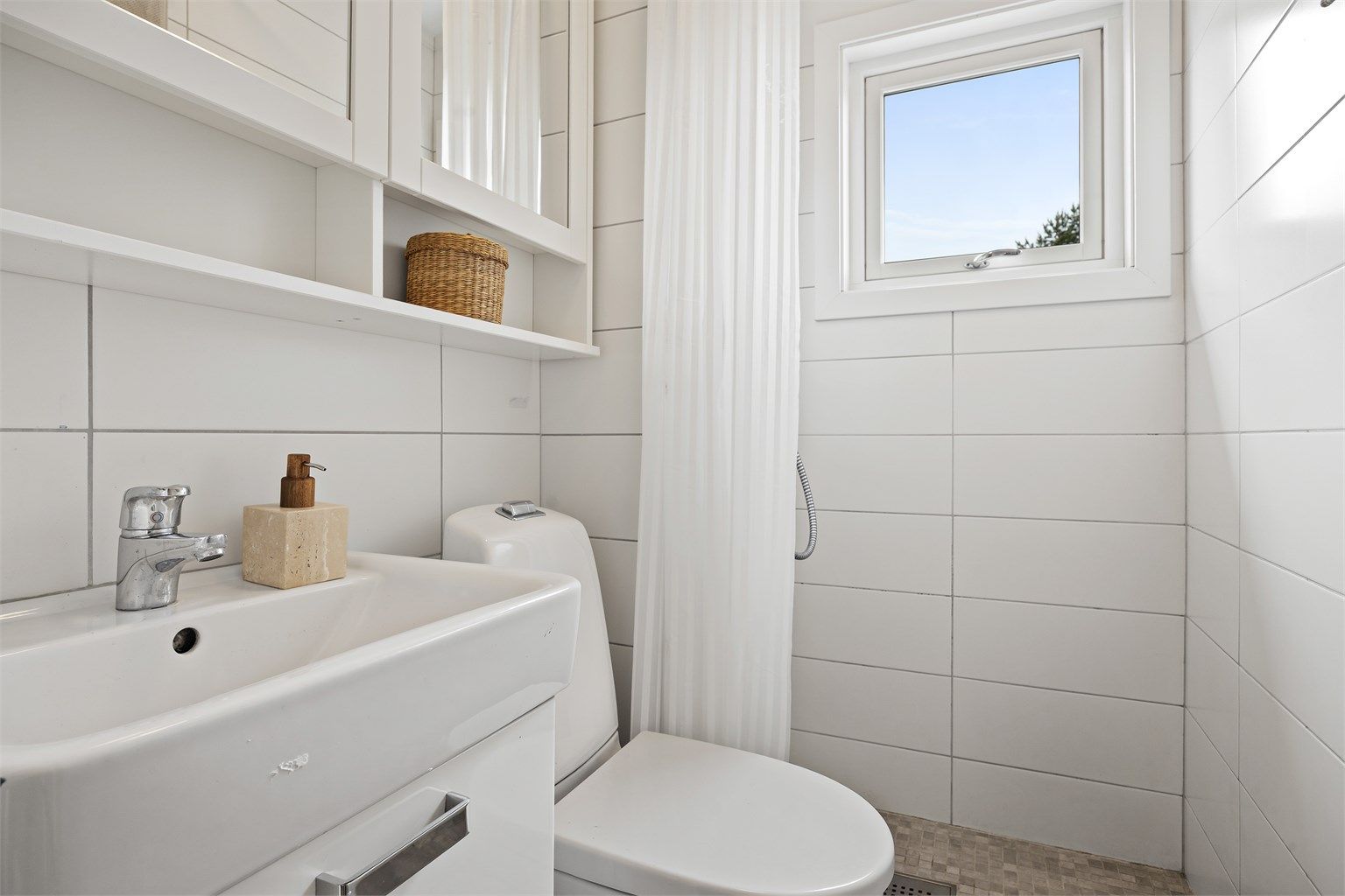 Badet har dusjhjørne med veggmontert regnfallsdusj og opplegg for dusjforheng.