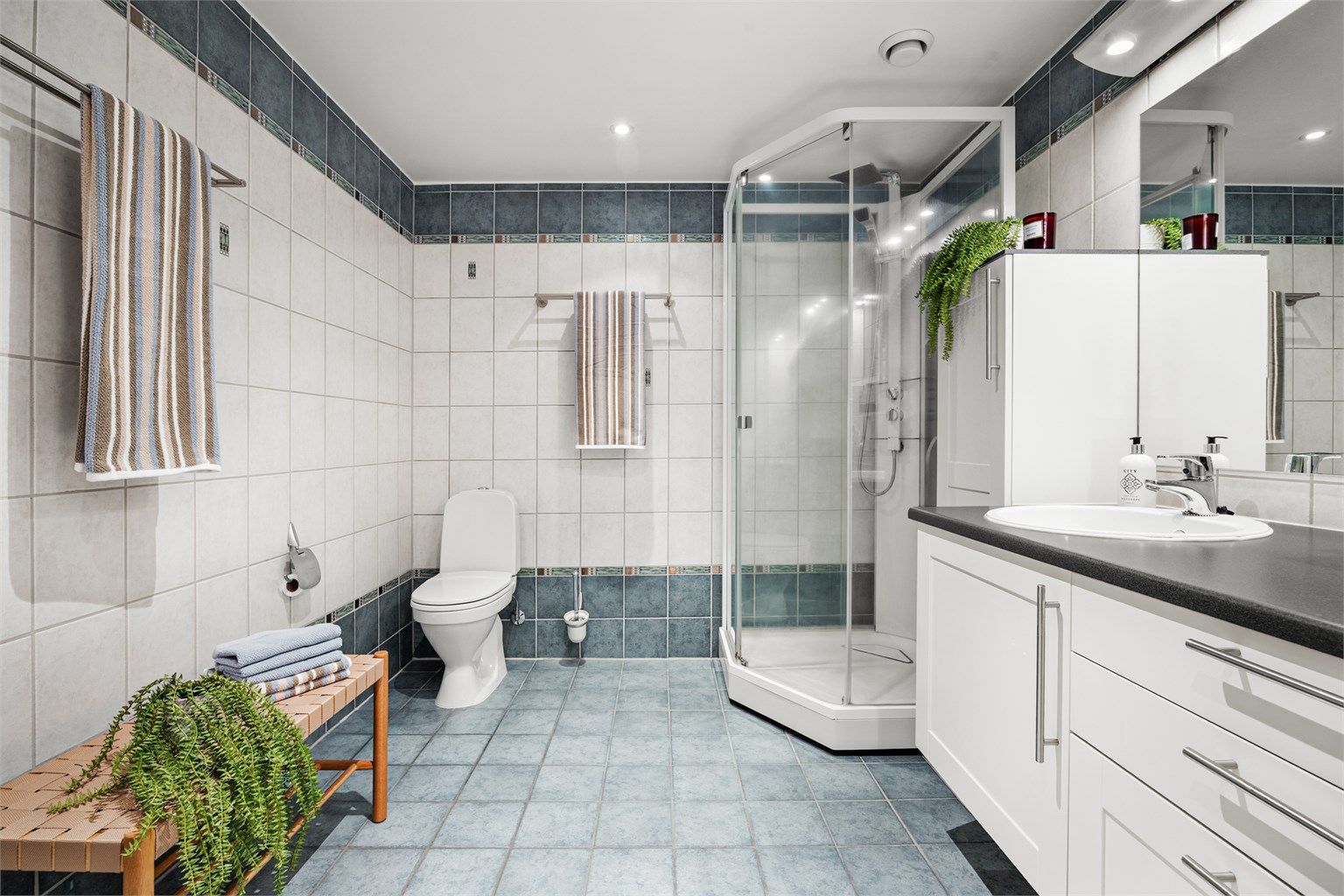 Badet er fra byggeåret og har flislagt gulv med varmekabler, dusjkabinett og downlights i himlingen.