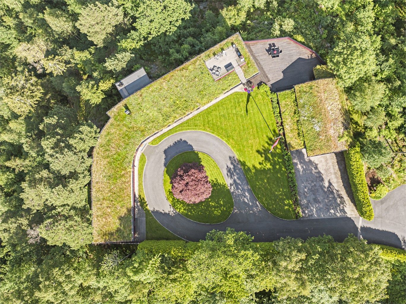 Tomten er rålekker med plen, asfaltert, privat rundkjøring, brostein og diverse beplantning, samt terrasser.