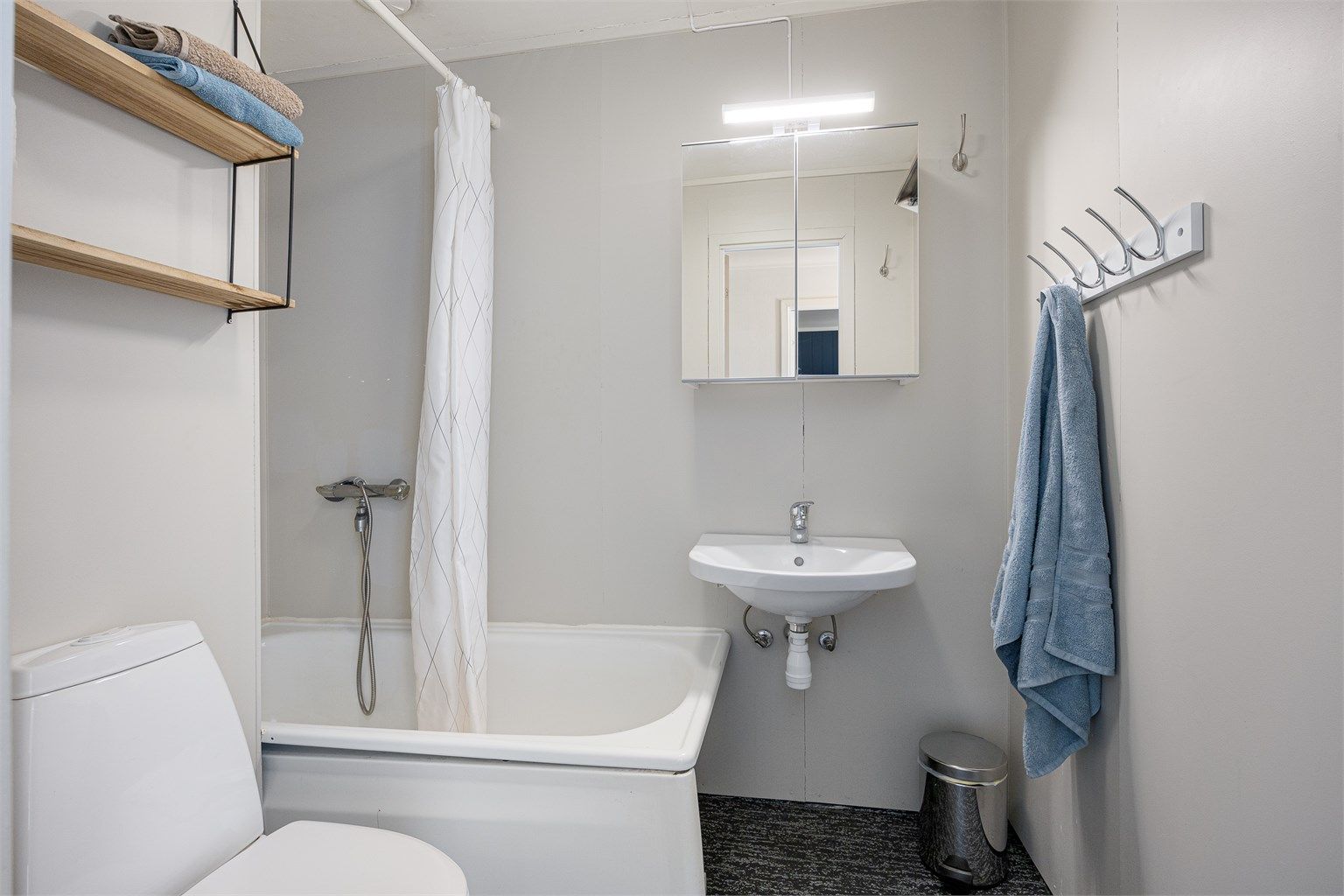 Badet er utstyrt med badekar, veggmontert servant, speilskap og toalett.