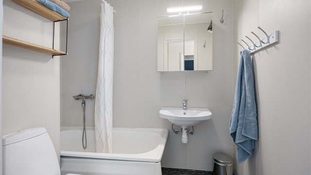Badet er utstyrt med badekar, veggmontert servant, speilskap og toalett.