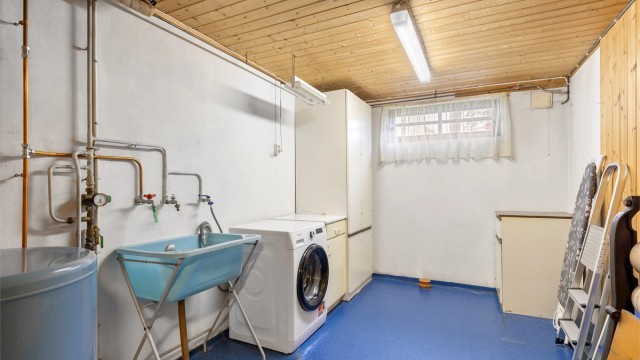 Stort vaskerom i kjeller med opplegg for vaskemaskin, varmtvannsbereder, utslagsvask og eldre vaskeromsinnredning