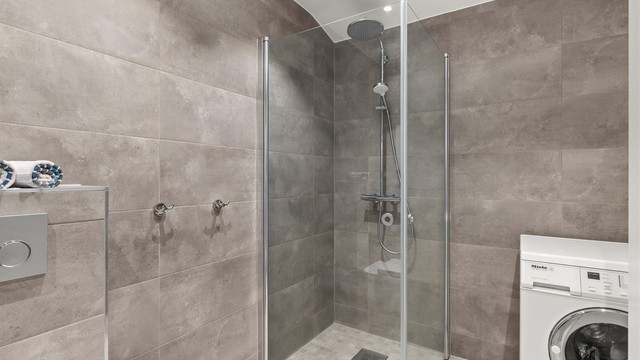 Badet er videre utstyrt med vegghengt toalett, et romslig dusjhjørne med glassdører og opplegg for vaskemaskin.