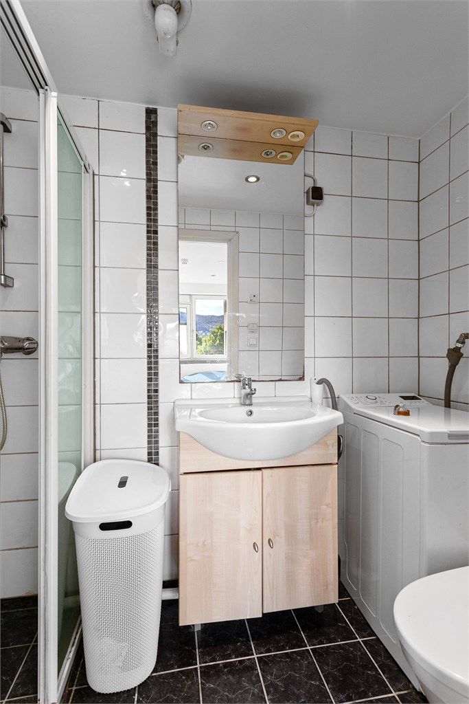 Badet har dusjnisje med skyvedørsramme og opplegg for smal vaskemaskin.