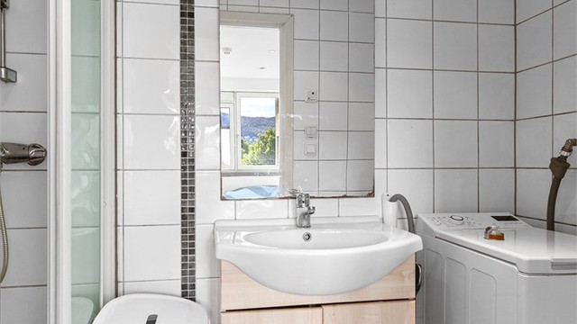 Badet har dusjnisje med skyvedørsramme og opplegg for smal vaskemaskin.