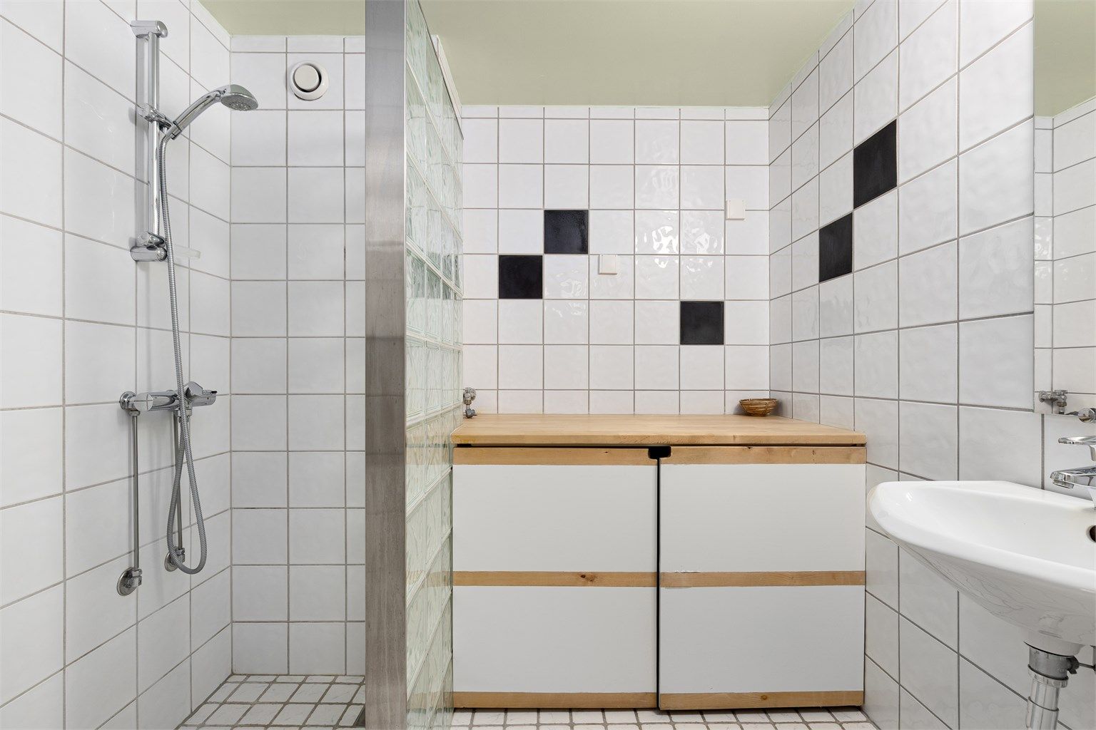 Pent flislagt baderom innredet med servant og dusjsone som er avskjermet med glassbyggerstein