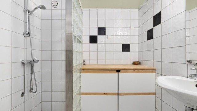 Pent flislagt baderom innredet med servant og dusjsone som er avskjermet med glassbyggerstein