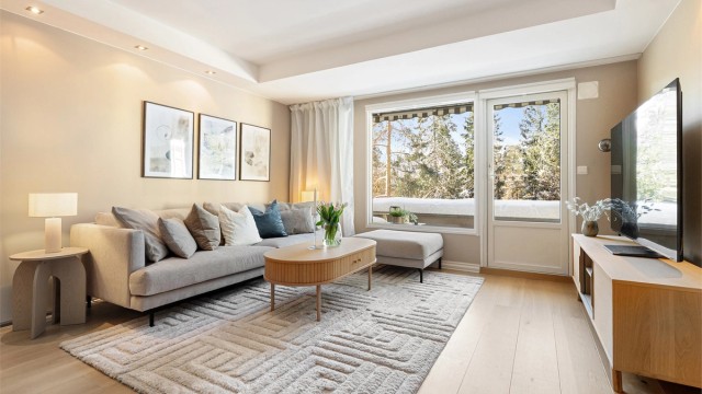 Stuen har glatte, malte flater, gjennomgående parkettgulv og store vinduer som gir en usjenert atmosfære uten innsyn.