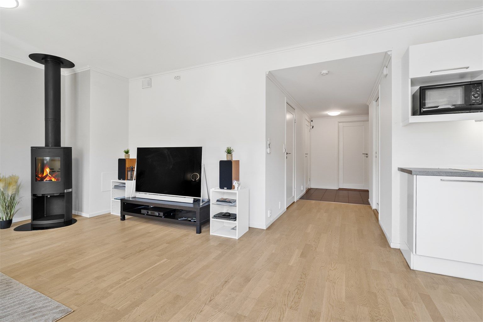 Lys og åpen stue med parkett på gulv, malte flater og peisovn som gir ekstra varme og stemning. Åpen løsning mot kjøkken