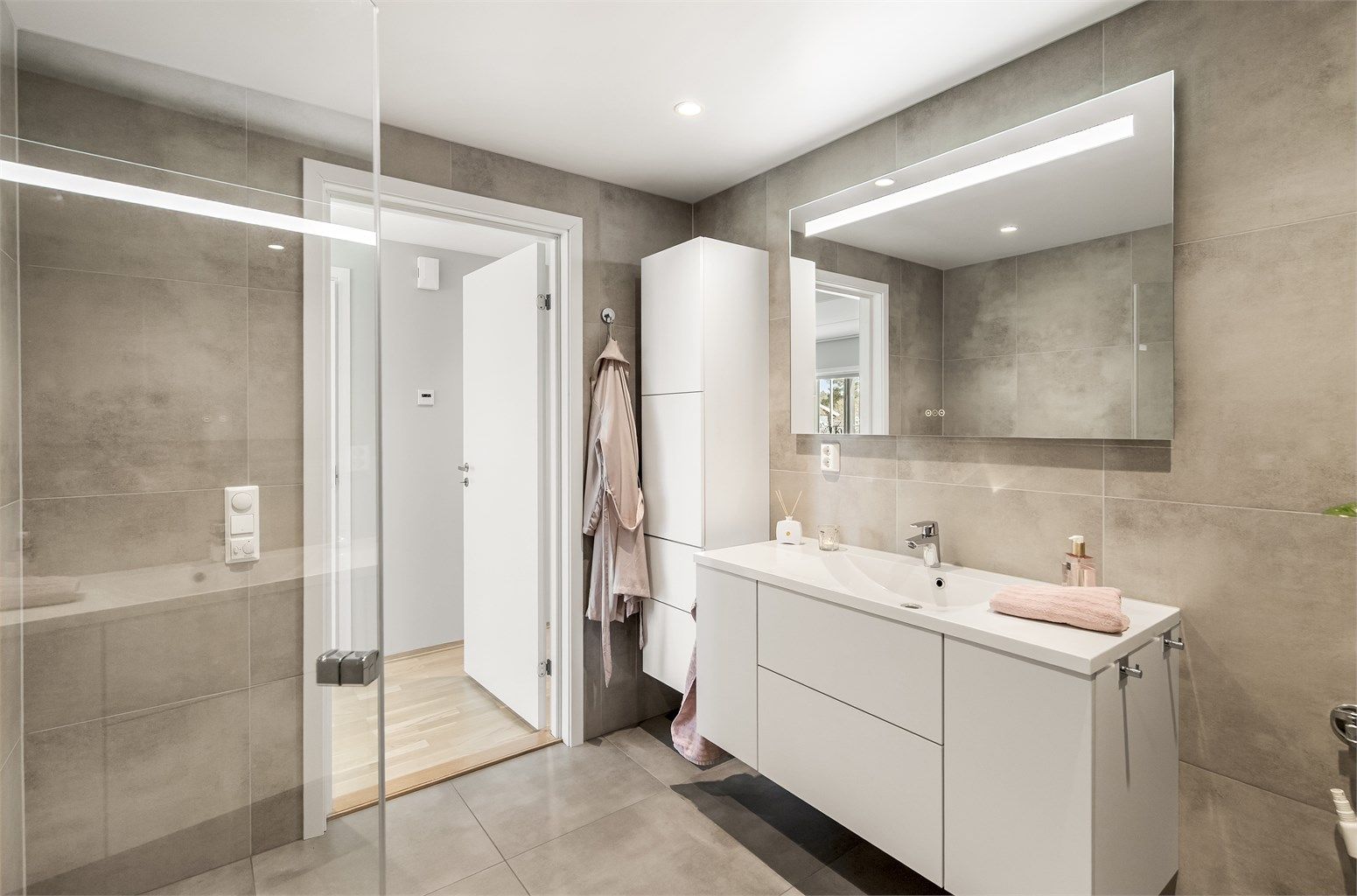 Badet har vegghengt toalett, dusjhjørne med glassdører og opplegg for vaskemaskin.