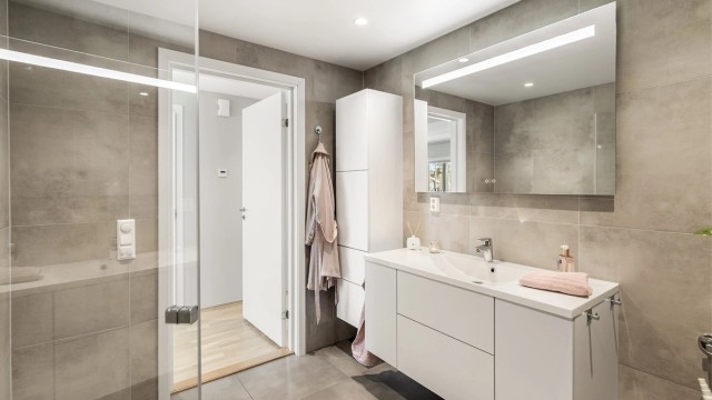 Badet har vegghengt toalett, dusjhjørne med glassdører og opplegg for vaskemaskin.