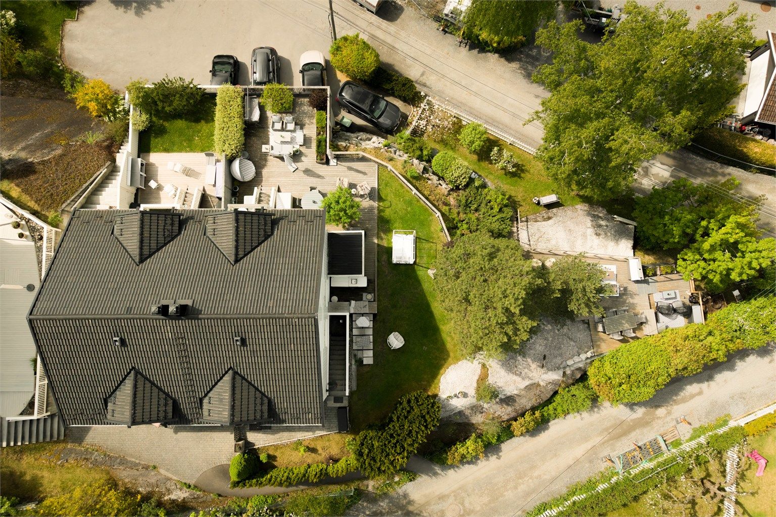 Oversikt over eiendommen som viser den store terrassen, hagen og garasjeanlegget.