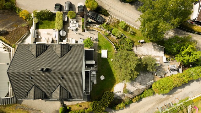 Oversikt over eiendommen som viser den store terrassen, hagen og garasjeanlegget.