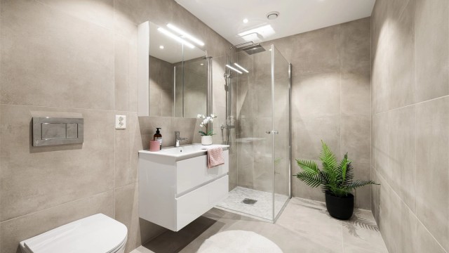 Lekre storformat fliser på både gulvet og veggene gir badet en visuell helhet. Dusjhjørnet er utstyrt med både hånd- og regndusj.