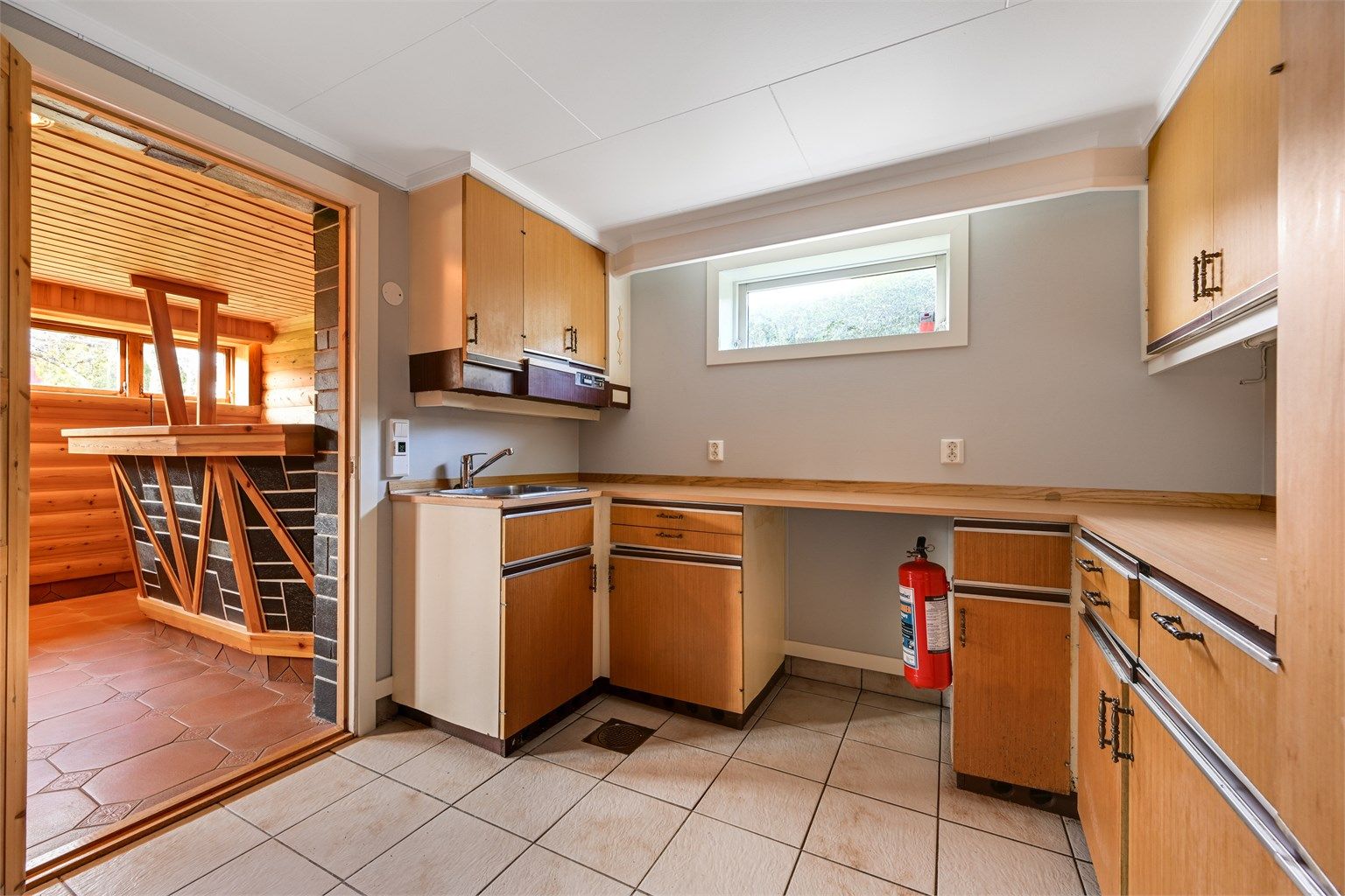 Innredet rom i kjelleren med kjøkkeninnredning. Boligens nye varmtvannstank fra 2024 er plassert her. (Ikke godkjent til varig opphold)