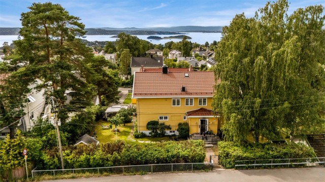 Hel tomannsbolig over fire plan med stor hage, verandaer og sjøutsikt.