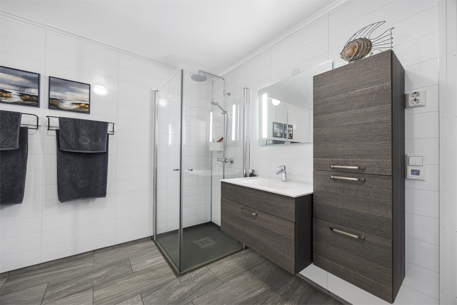 Stort bad innredet med servant og baderomsoppbevaring, dusjhjørne, vegghengt toalett og opplegg til vaskemaskin. Flislagt gulv med varmekabler. 