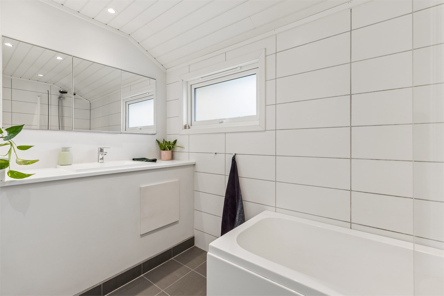 Pent baderom med flislagte vegger- og gulv med gulvvarme, samt skråtakshimling i MDF-paneler med downlights. 