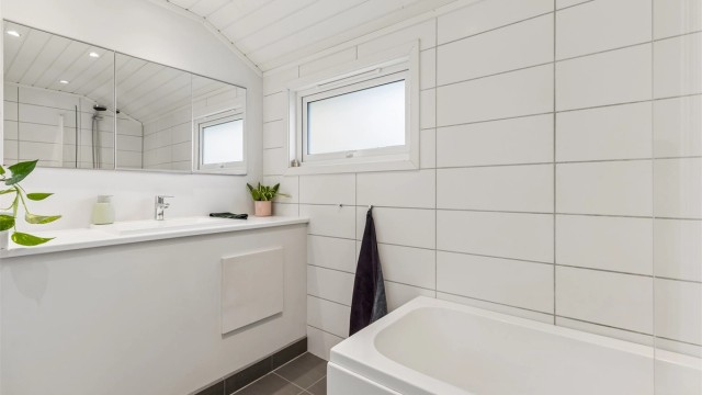 Pent baderom med flislagte vegger- og gulv med gulvvarme, samt skråtakshimling i MDF-paneler med downlights.