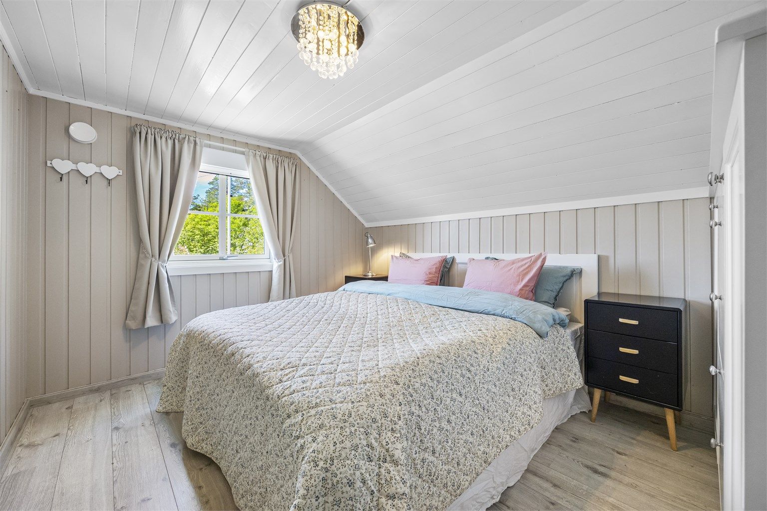 Boligens andre soverom på loftet, med laminat på gulvet og malt panel.