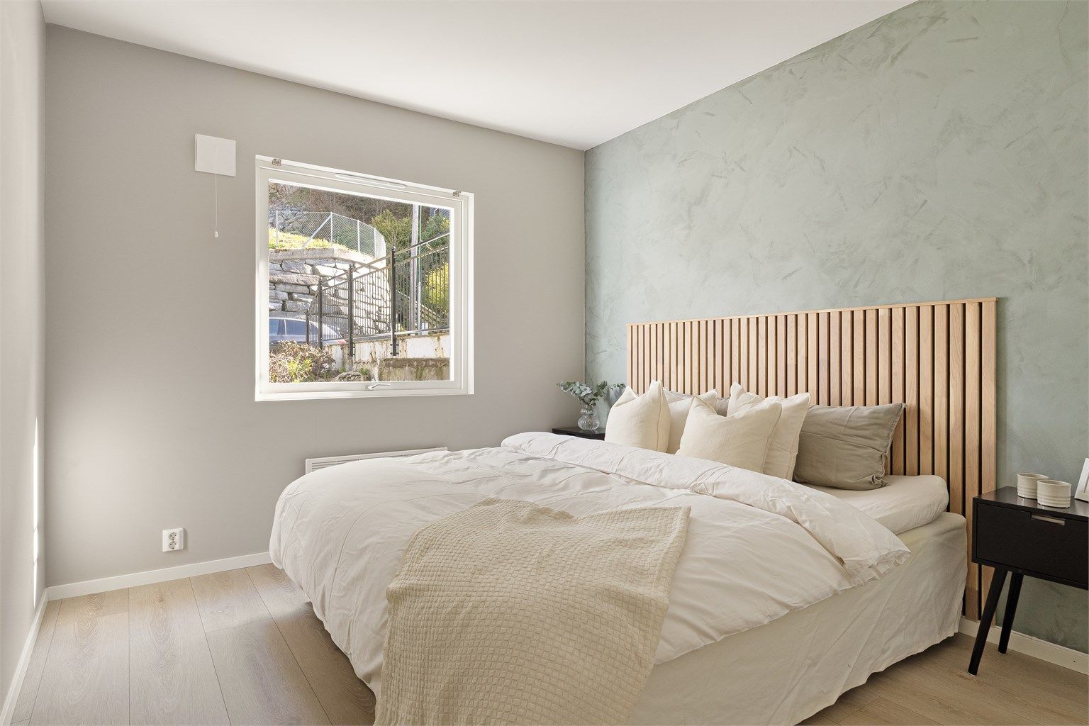 Innbydende soverom med lysmalte overflater og en superfin eikefarget sengegavl.