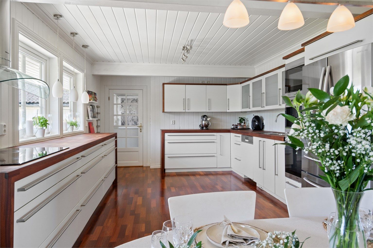 Innredningen er montert langs flere sider og har lyse, glatte fronter, frostede vitrineskap og treveggmonterte høyskap med vitrinedører i spisesonen.