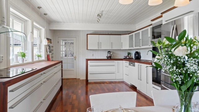 Innredningen er montert langs flere sider og har lyse, glatte fronter, frostede vitrineskap og treveggmonterte høyskap med vitrinedører i spisesonen.