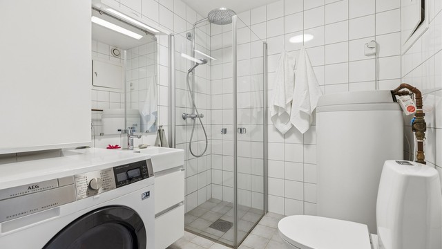 Lyst og delikat flislagt bad med dusjhjørne med innadslående glassdører er både funksjonelt og stilfullt, samtidig som det sparer plass.
