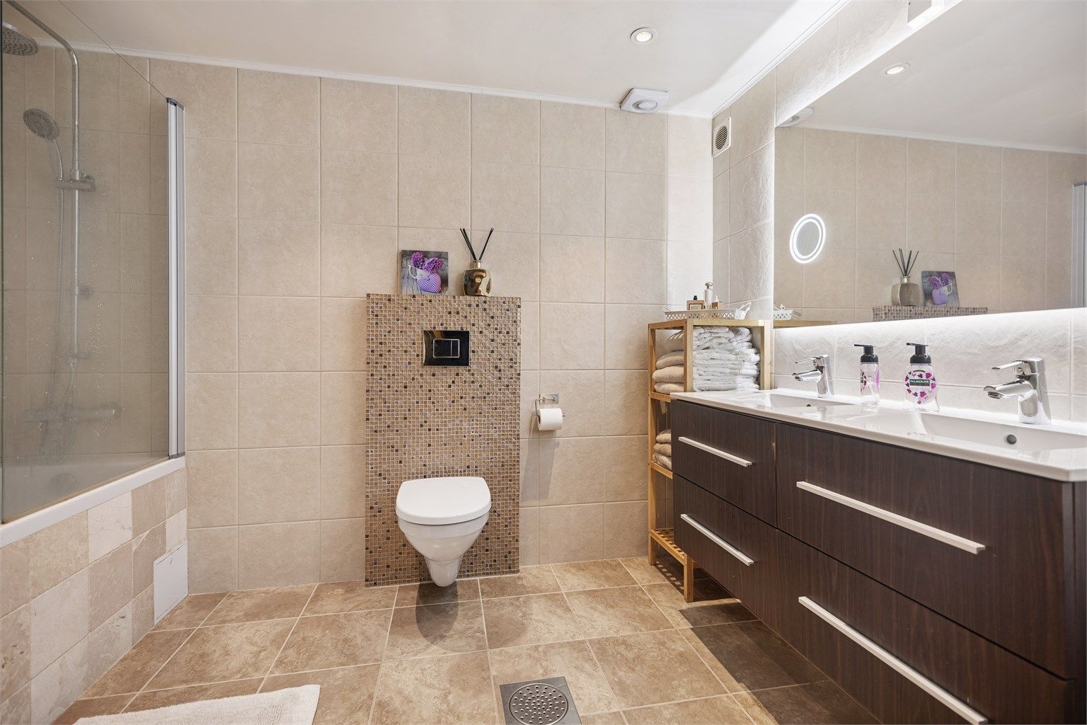 Baderommet fremstår som et romslig og lekkert velværebad med gjennomførte materialvalg og god plass. Varmekabler i gulvet sørger for behagelig komfort året rundt, og gjør rommet både praktisk og innbydende