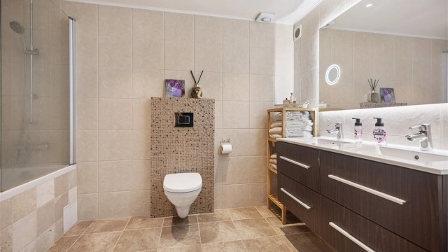 Baderommet fremstår som et romslig og lekkert velværebad med gjennomførte materialvalg og god plass. Varmekabler i gulvet sørger for behagelig komfort året rundt, og gjør rommet både praktisk og innbydende