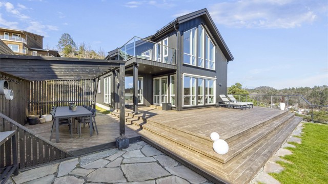 Boligen har en moderne arkitektur med stående trekledning og store vindusflater.