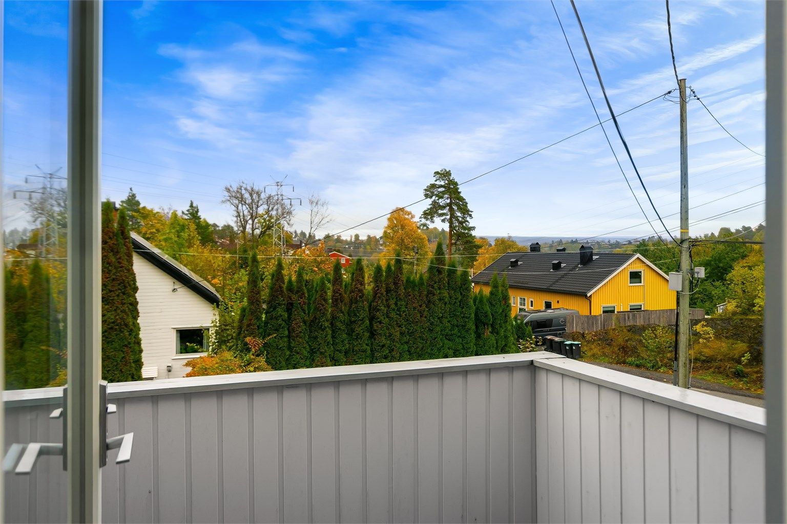 Utsyn fra balkongen over grønne nærområder og tomten.